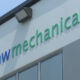 Exterior wall sign reading 'nw mechanical' in green and blue letters, with a logo on the left and an outdoor light above.