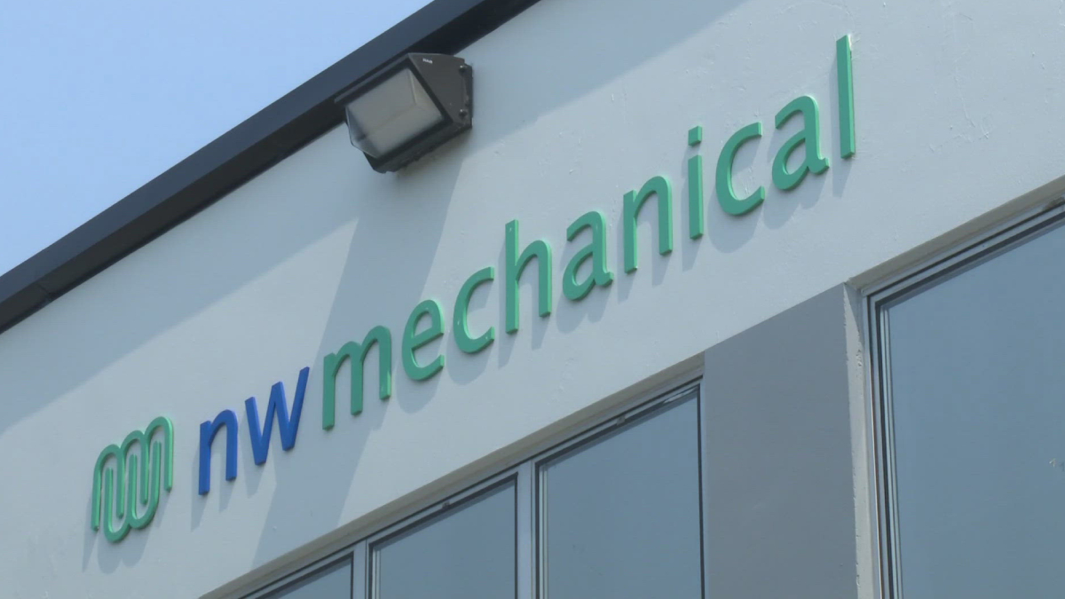 Exterior wall sign reading 'nw mechanical' in green and blue letters, with a logo on the left and an outdoor light above.