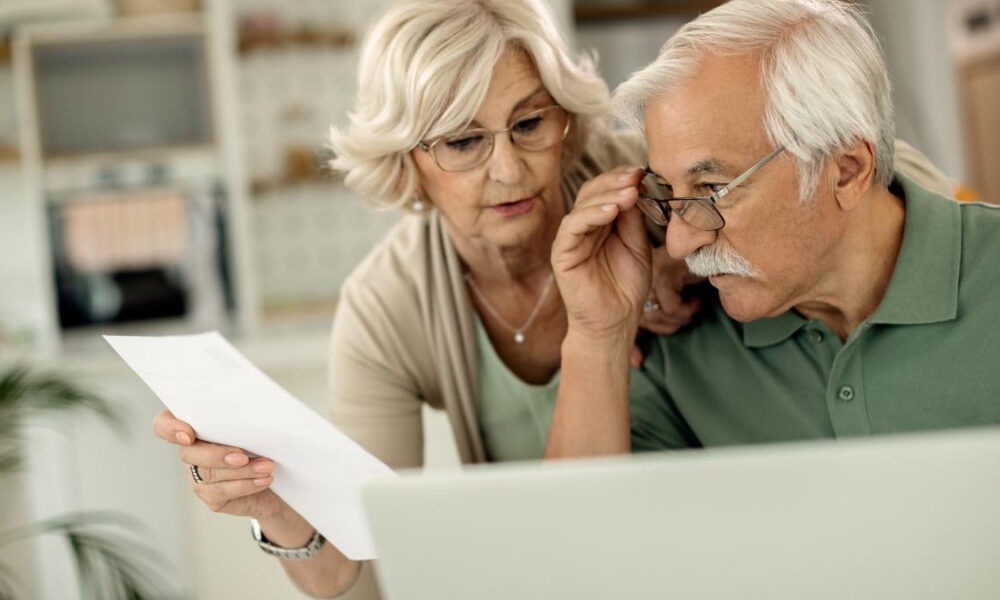 Older couple reviewing a document together beside a laptop at home.