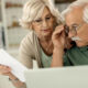 Older couple reviewing a document together beside a laptop at home.