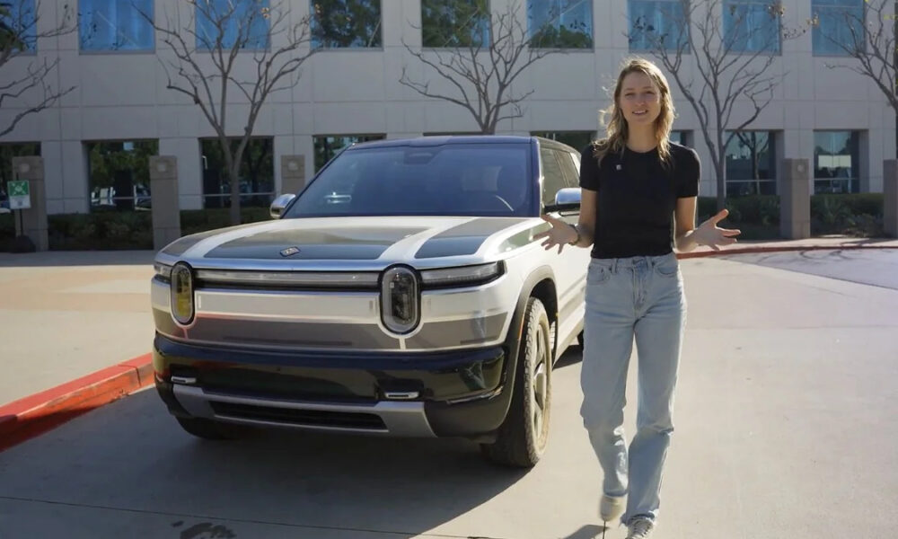 Woman standing beside a white SUV in a parking lot outside a modern office building, gesturing with open hands.