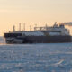 Icebreaker Boris Davydov sailing through a frozen Arctic sea at sunset, exhaust plume trailing behind.
