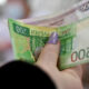 Close-up of a hand with purple nail polish holding and counting Polish zloty banknotes.