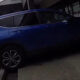 Blue SUV parked on a curbside next to a storefront with its rear hatch open.