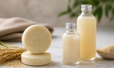Round cheese wheels stacked on a marble surface with two glass bottles of milk and grains nearby in a kitchen setting.