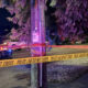 Nighttime police scene with yellow 'POLICE LINE DO NOT CROSS' tape and a patrol car with blue flashing lights.