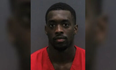 Mugshot of a man in a red jumpsuit facing the camera with a neutral expression against a gray backdrop.