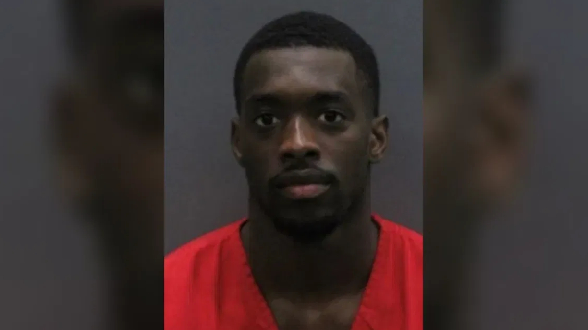 Mugshot of a man in a red jumpsuit facing the camera with a neutral expression against a gray backdrop.
