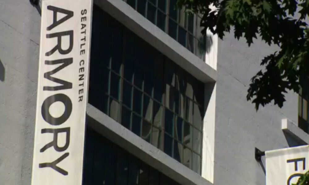 Vertical banner on a gray building reading 'ARMORY' with 'SEATTLE CENTER' text, against windows and tree branches in the foreground.