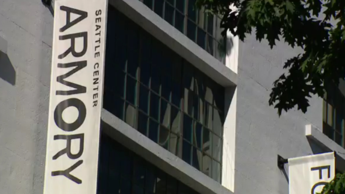 Vertical banner on a gray building reading 'ARMORY' with 'SEATTLE CENTER' text, against windows and tree branches in the foreground.