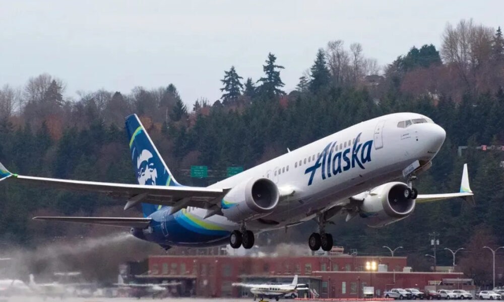 Alaska Airlines plane lifting off from a runway with a forested backdrop behind it.