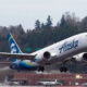 Alaska Airlines plane lifting off from a runway with a forested backdrop behind it.
