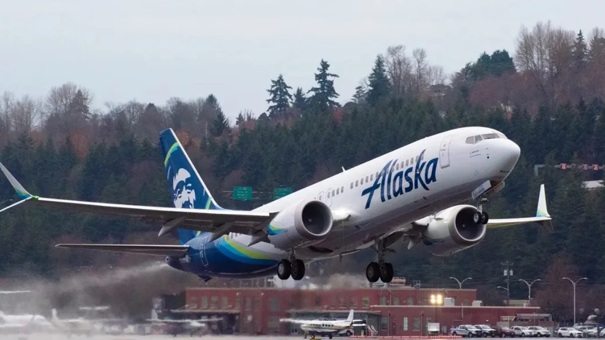 Alaska Airlines plane lifting off from a runway with a forested backdrop behind it.