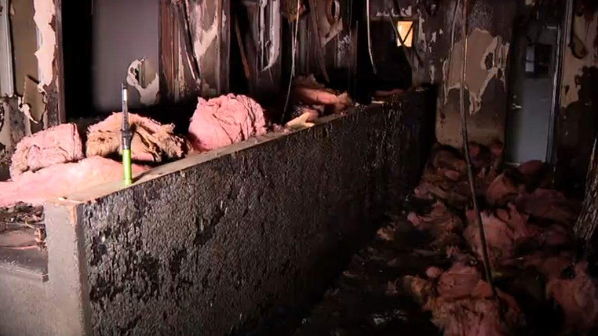 Charred interior with pink insulation on a ledge, burned walls, and debris on the floor near a green tool.