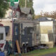 Row of weathered campers and scattered junk in a residential yard beside a street corner.",