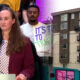 Woman in a maroon blazer speaks at a podium with a microphone, addressing an audience of supporters behind her; urban street scene to the right.