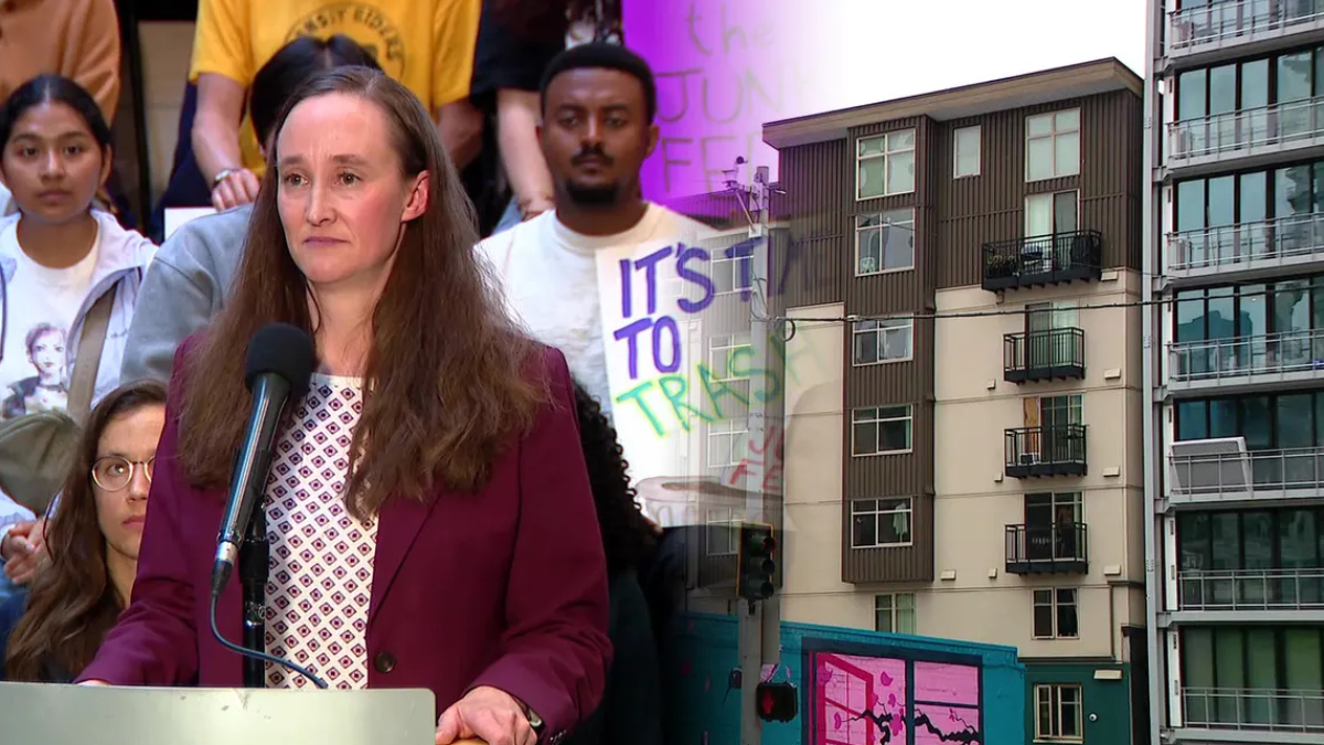 Woman in a maroon blazer speaks at a podium with a microphone, addressing an audience of supporters behind her; urban street scene to the right.