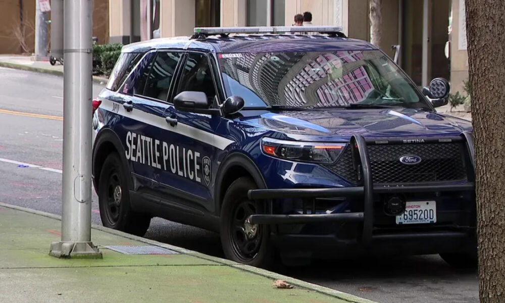 Seattle Police SUV with front bumper guard parked at curb on an urban street; city reflections in windows.