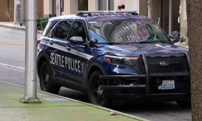 Seattle Police SUV with front bumper guard parked at curb on an urban street; city reflections in windows.