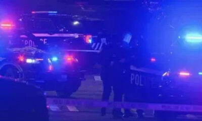 Police cars with flashing blue lights at night, police tape across a street, and officers on a dimly lit scene.