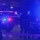 Police cars with flashing blue lights at night, police tape across a street, and officers on a dimly lit scene.