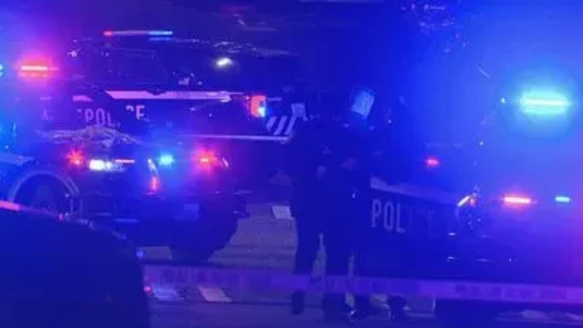 Police cars with flashing blue lights at night, police tape across a street, and officers on a dimly lit scene.