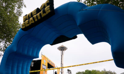 Large blue inflatable arch forms a finish line gate at an outdoor Seattle event, with the Space Needle visible in the background and caution tape across the area.