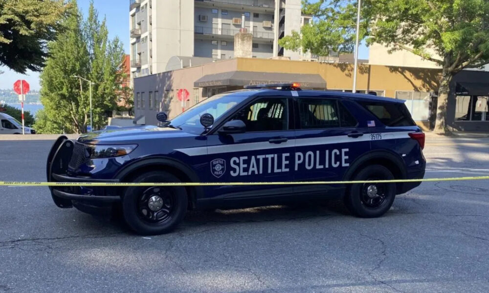 Seattle Police SUV behind yellow caution tape on a city street, with buildings and trees in the background