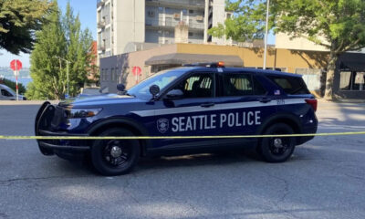 Seattle Police SUV behind yellow caution tape on a city street, with buildings and trees in the background