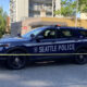 Seattle Police SUV behind yellow caution tape on a city street, with buildings and trees in the background