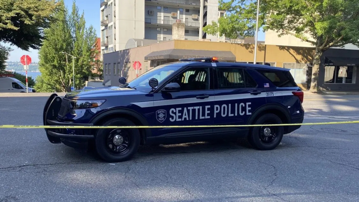 Seattle Police SUV behind yellow caution tape on a city street, with buildings and trees in the background