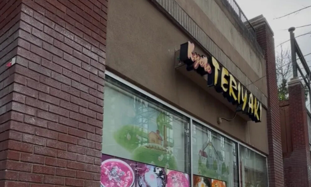 Exterior view of a bakery storefront with large glass windows showing colorful cake displays and a stylized sign above the entrance.