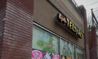 Exterior view of a bakery storefront with large glass windows showing colorful cake displays and a stylized sign above the entrance.