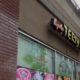 Exterior view of a bakery storefront with large glass windows showing colorful cake displays and a stylized sign above the entrance.