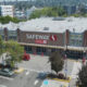 Aerial view of a Safeway supermarket with large front sign, surrounding parking lot, and striped pedestrian crosswalks outside the entrance.
