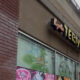 Exterior view of a brick storefront with a sign that appears to say 'Teriyaki' above large display windows with colorful food posters inside.