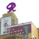 Neon red R sign atop a retro Rainier beer building with banners reading 'The Old Rainier Brewery' and 'It's R Light Beer'.