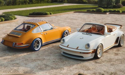 Two vintage Porsche convertibles parked on a gravel driveway with neatly trimmed shrubs in the background.