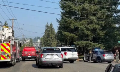 Fire truck and red emergency vehicle block a residential street as responders work behind police tape.