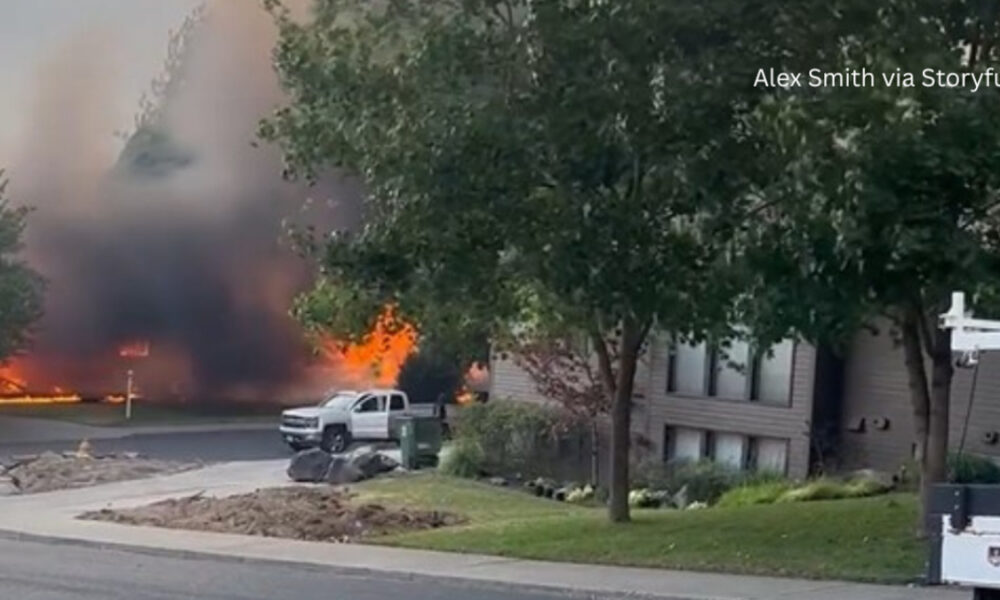 Residential street fire with large flames and dark smoke behind a parked white pickup truck.