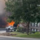 Residential street fire with large flames and dark smoke behind a parked white pickup truck.