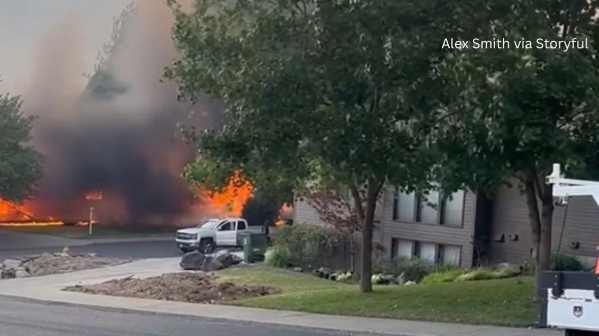 Residential street fire with large flames and dark smoke behind a parked white pickup truck.