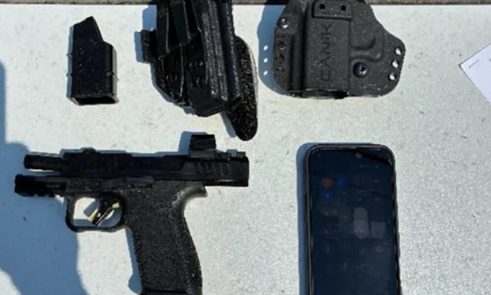 Semi-automatic pistol with a magazine, holster, and a smartphone on a gray surface.