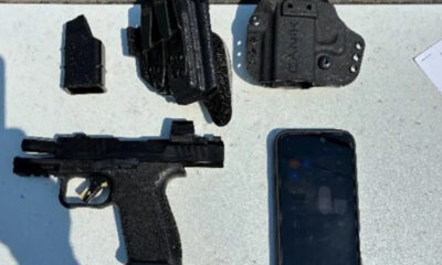 Semi-automatic pistol with a magazine, holster, and a smartphone on a gray surface.