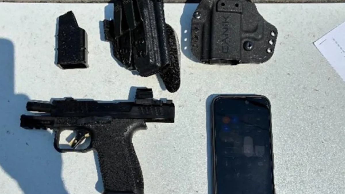 Semi-automatic pistol with a magazine, holster, and a smartphone on a gray surface.
