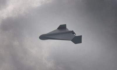 White unmanned aerial vehicle (drone) with swept wings flying through a cloudy sky.