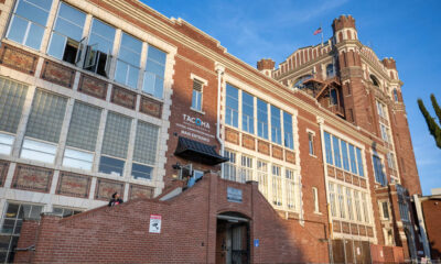 Brick, multi-story building with a tall tower on the right, large windows, and brick stairs leading to a main entrance under a small canopy. A U.S. flag waves atop the tower.