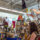 Cluttered art shop interior with a graffiti-covered wall, hanging props, and a woman browsing the displays.