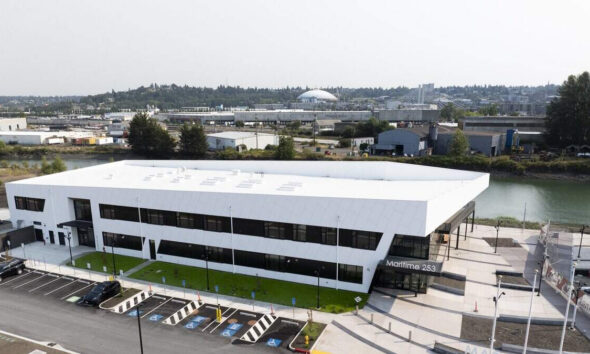 Aerial view of a modern white two-story office building by a waterway, with a parking lot and accessible parking spaces in front.