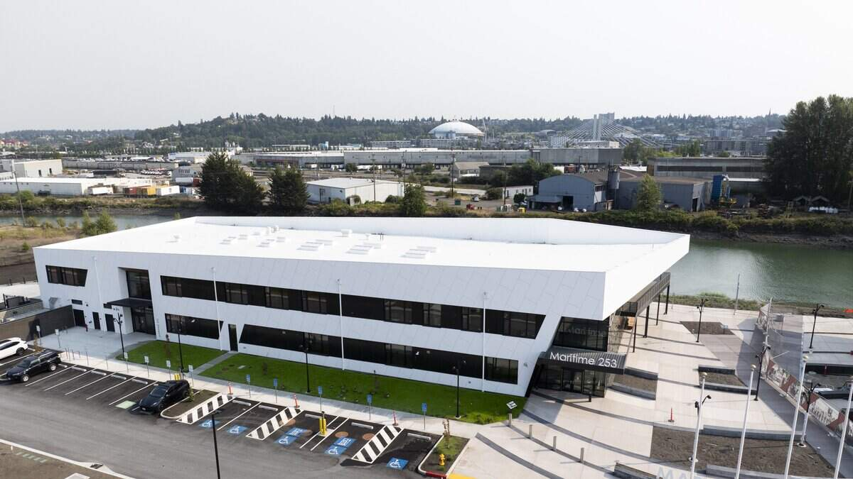 Aerial view of a modern white two-story office building by a waterway, with a parking lot and accessible parking spaces in front.